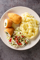 Chicken Kiev is a dish made of chicken cutlet stuffed with butter abd herbs served with salad and mashed potatoes closeup in the plate on the table. Vertical top view from above