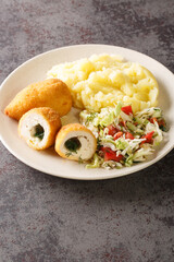 Chicken Kiev is a dish made of chicken cutlet stuffed with butter abd herbs served with salad and mashed potatoes closeup in the plate on the table. Vertical 