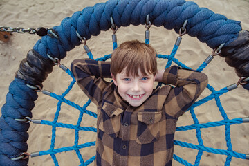 Adorable little child boy smiling happily, riding on a blue round hanging swing on the playground....