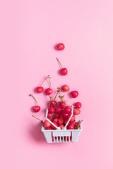 A handful of cherries scattered from a cart, sweet cherries on a pink background. Vertical photo