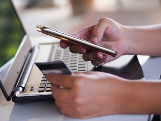 Closeup hands using smartphone and credit card paying online at home office.