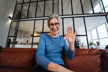 Middle Aged Woman Smiles and Waves to the Camera, Looking at Camera.