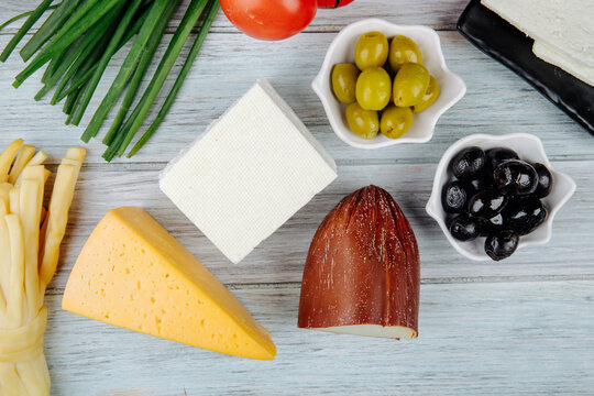 Top View Of Different Kinds Of Cheese With Green Onion And Pickled Olives On Grey Wooden Background