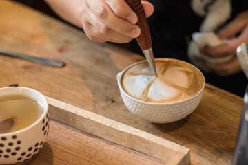 The barista uses his hands to decorate the milk froth on the cup of coffee latte.