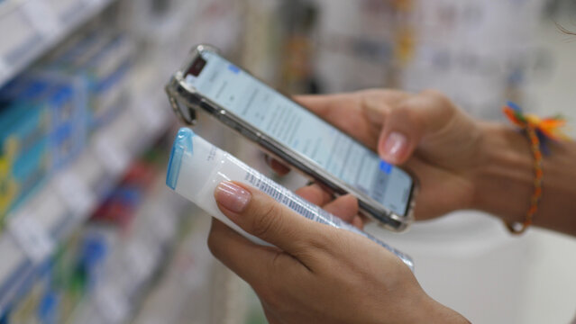 Woman Reading Product Label In Cosmetics Shop Using Mobile Phone Checking Components. Close up. 4K.