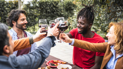 family party with adoptive parents and children to celebrate the achievements of the young student of African descent, mixed age range people toasting with red wine glasses at barbecue