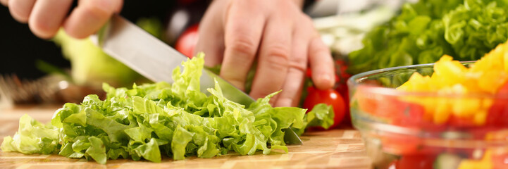 A male chef cuts a green salad with a knife