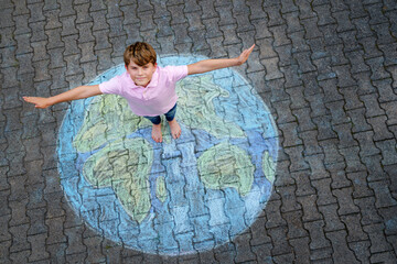 Little school boy with earth globe painting with colorful chalks on ground. Positive kid child....