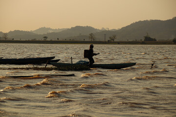 Sunset silhouettes of a fisherman among the boats in Lak Lake in the township of Lien son, Dak Lak Vietnam