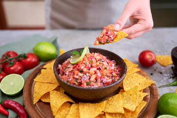 freshly made salsa dip sauce with nacho chips on wooden board