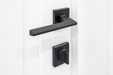 Modern black door handle on white wooden door in interior. Knob close-up elements. Door handle, fittings for interior design