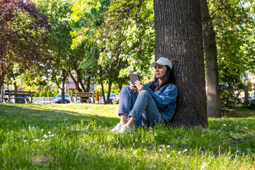 Naklejka na ściany i meble woman sitting under the tree reading electronic book