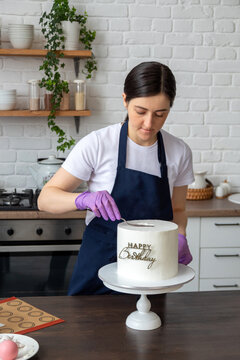 Pastry chef in an apron lines the cream on birthday cake. Selective focus. Photos about confectioners, food, hobbies.