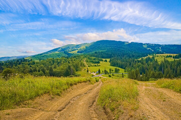 Naklejka premium Beautiful field with dirt road and forest, covered with hills behind the mountain and the sky with barns. landscape background.
