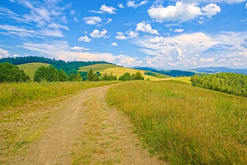 Fototapeta na wymiar Beautiful field with a dirt road on a hill, hills covered with grass behind the mountains and the sky with barns. landscape background.