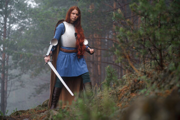 Young red-haired girl in medieval knight's armor in summer forest. Fantasy concept