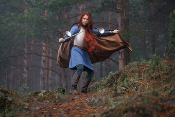 Fototapeta premium Young red-haired girl in medieval knight's armor in summer forest