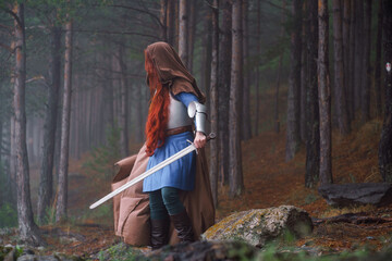 Red-haired girl in armor and raincoat in forest. Historical concept