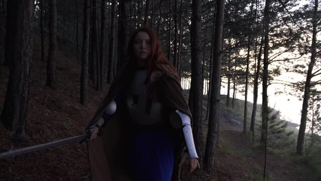 Young red-haired girl in medieval knight's armor in summer forest