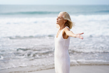 Mature female opening her arms on the beach, spending her leisure time, enjoying her free time