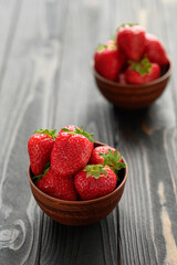 A bowl of red juicy strawberries on rustic wooden table. Healthy and diet snack food concept.