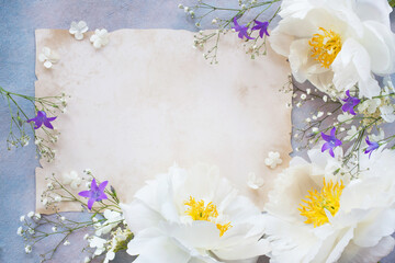 Decorative background with white peonies, bluebell flowers, gypsophila and paper for writing and text congratulations on the holiday
