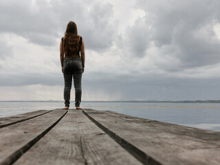  teenage girl stands looking out into the overcast sky. the concept loneliness