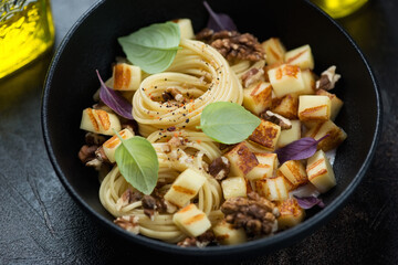 Creamy spaghetti served with chopped grilled halloumi and walnuts in a black bowl, close-up, horizontal shot, selective focus