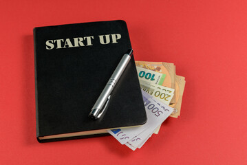 Start up . Accounting black book, euro banknotes and pen on red background