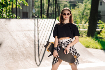 Teenager skater girl holding a skateboard an standing in the skaters park
