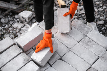 a male builder in a hard hat and protective gloves unloads bricks at a construction site