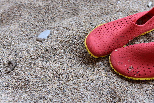 flip flops on the sand.close up photo of red beach shoes made of large sand and rocks. A summer beach scene with red rubber shoes on a sandy surface.