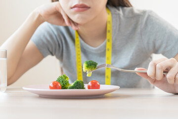 Anorexia, unhappy beautiful asian young woman, girl on dieting, hand holding fork at broccoli in salad plate, dislike or tired with eat fresh vegetables. Nutrition of clean, healthy food good taste.