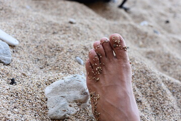 feet on the sand.A man's foot on a sand surface with small stones taped to it.lying foot in the sand facing upwards.