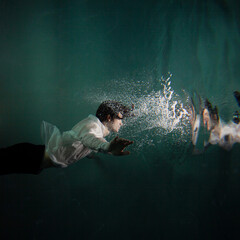 underwater shooting with contrasting light, a guy is swimming underwater, pulling his hand to his reflection in the surface of the water. Subconsciousness and self-reflection, concept - 511835272