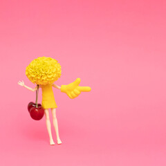Doll with marigold head holding beach bag made of cherries and showing pointer sign. Minimal summer style, food or vacation concept. Summertime!