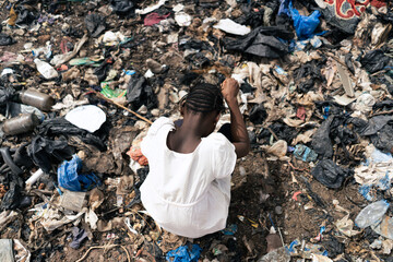 Top view of an African girl surrounded by trash looking for recyclable material - obrazy, fototapety, plakaty