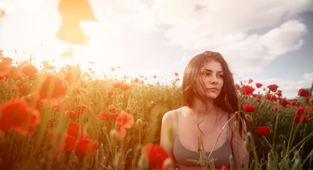 Obraz na płótnie Canvas Portrait of a woman in the poppy field against strong sunlight