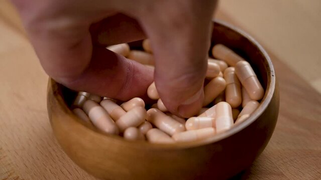A hand takes a capsule of vitamin B complex from a full wooden eco bowl close-up in slow motion. Avitaminosis concept