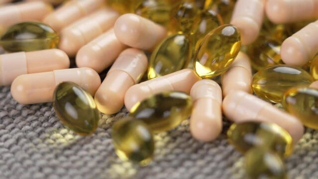 Mix of capsules of vitamin B complex and omega 3 pills close-up on a gray rough cloth. Rotation. Avitaminosis idea