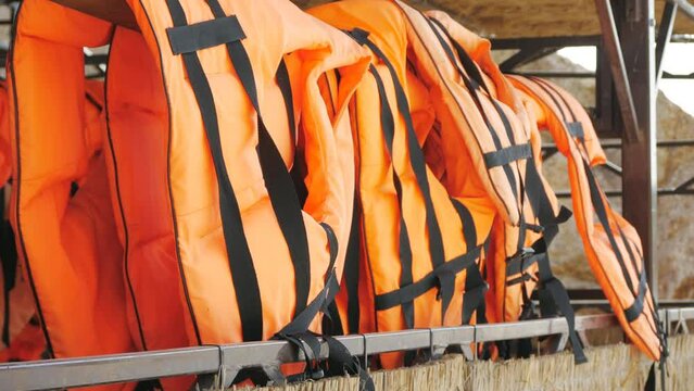 Orange life jackets in store by the sea. Many life jackets hang in a row on hangers. Protective safety clothing at rental boat store.