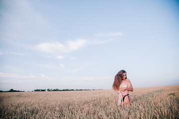 A young, slender, in black panties in a field of wheat covers her chest with a straw hat.