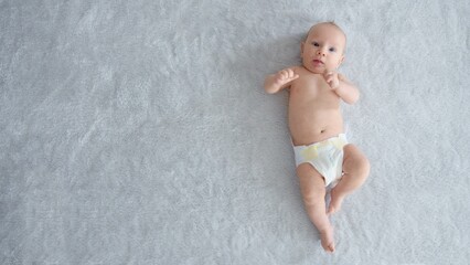 A healthy newborn baby in a diaper without clothes, top view. Full length . Happy newborn boy lies on a blue blanket and actively moves his arms and legs. Cute baby with blue eyes