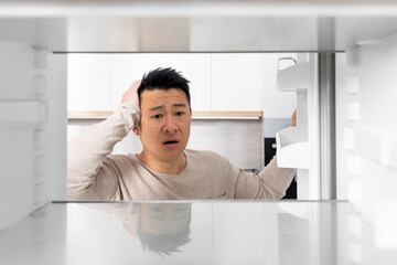 Shocked chinese man looking inside empty fridge