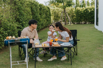 Asian family having dinner in the backyard at home. Happy family with little child camping and have fun in house backyard outside. Barbecue time, Family activities conccept.