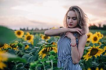 Young, slender, with loose hair in a field of sunflowers at sunset