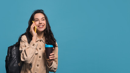 Smiling millennial caucasian female brunette in casual with backpack hold coffee cup takeaway and talking on phone
