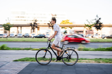 Obraz premium Young modern man riding bicycle on city streets, motion blur, panning shot, summer time