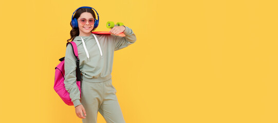 Happy teenager in activewear holding pennyboard yellow background, board skating. Casual teen child horizontal poster. Banner header, copy space.