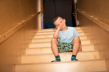 A cute calm boy is sitting on a wooden ladder.